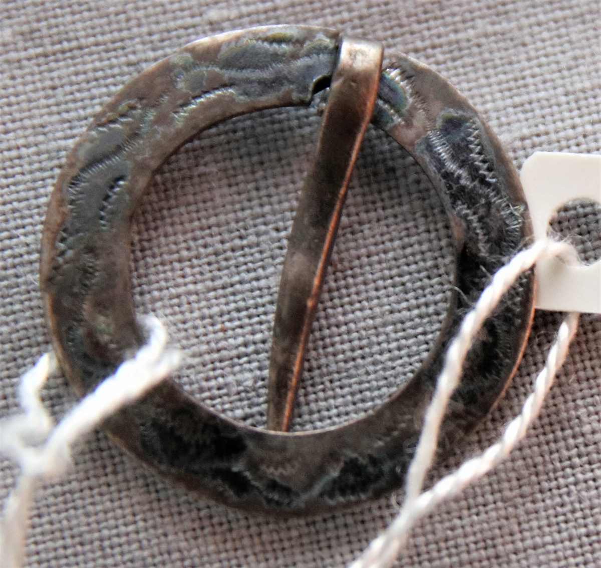 Brosch i silver (L4=1841, svårtydda stämplar), cirkelrund med 4 mm bred silverplåt på översidan mönstrad med trampolerade våglinjer.