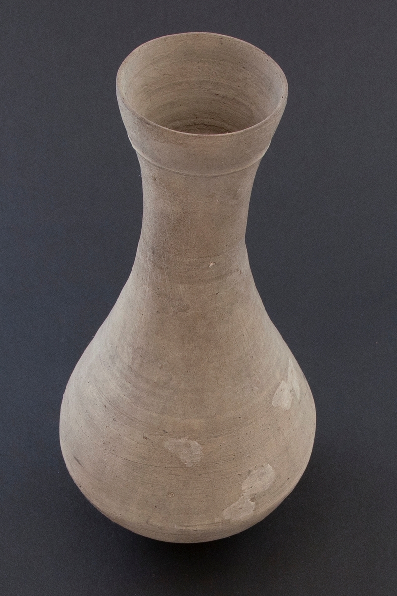 Balusterformet flaske med høy hals og lav fot. Flasken er dreid i gråbrunt leirgods og er uglasert.