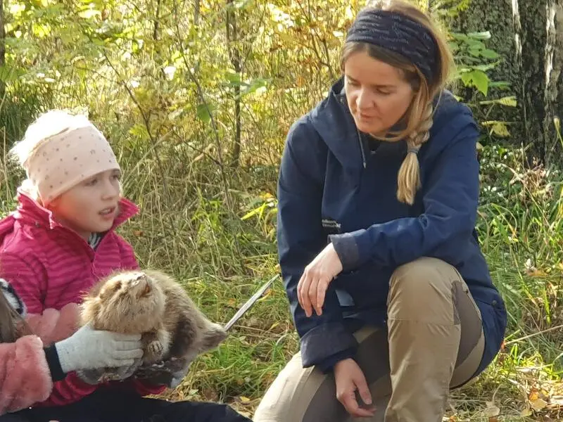 Foto av en naturveileder som sitter på huk og forteller et barn om en utstoppet bever som barnet holder