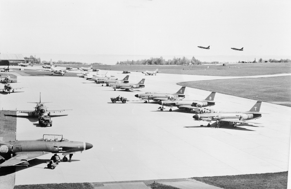 En division av flygplan A 32A Lansen uppställda på flygfältet på F6 i Karlsborg, omkring 1962-1965. Flygplan Tp 55 är på besök, I bakgrunden syns två flygplan A 32 som just har startat.
