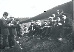 En gruppe yngre menn sitter og står i graskledd skråning. He