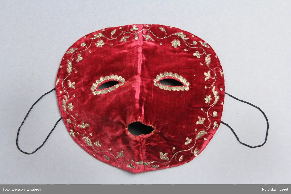 En rund mask av röd slät silkessammet med guldbroderier. Baksidan fodrad med tunt vävt linne- eller bomullstyg. Handsömnad rakt igenom. Daterad 1700-tal av textilintendent Ingrid Roos 2008.
Lena Kättström Höök 2012-12-13
