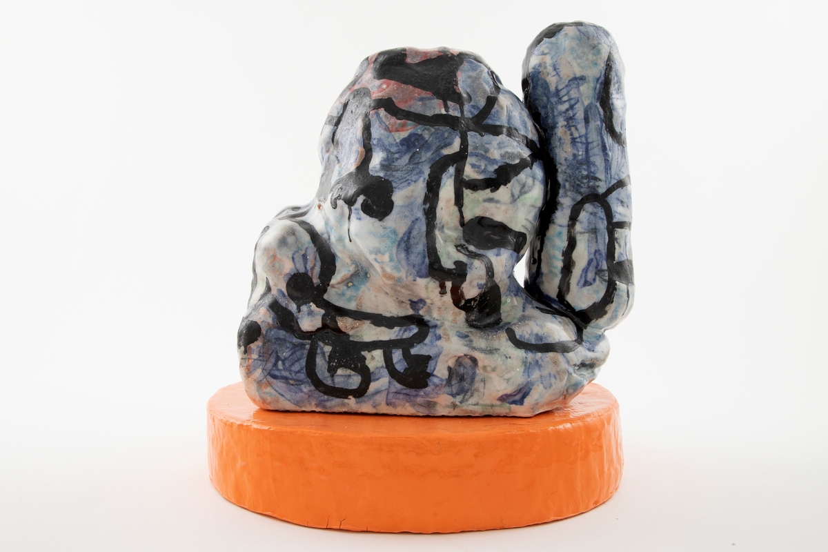 Skulptur i to deler. Frittstående abstrakt skulptur med blå, rosa og hvit glasur med svart nonfiguraiv glasurtegning. Skulpturen står på oval oransje base.