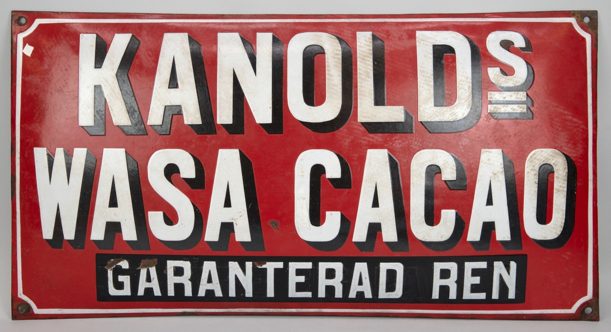Rektangulär reklamskylt av emaljerad plåt, kupad. Röd botten med vit text:
"KANOLDs 
WASA CACAO 
GARANTERAD REN"
Fyra hål i vardera hörn för uppsättning.