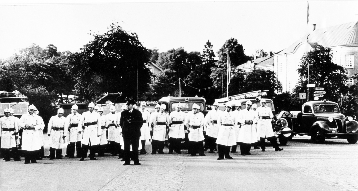 Brandkårens 50-års jubileum 1950. Brandmän och chef står uppställda framför sina brandbilar vid uppvisningen.