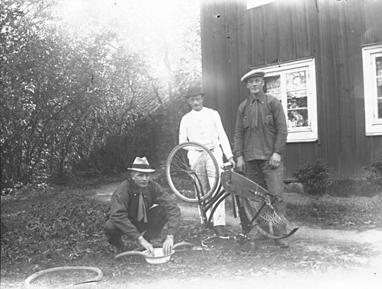 Grupporträtt, tre män lagar punktering på en cykel.