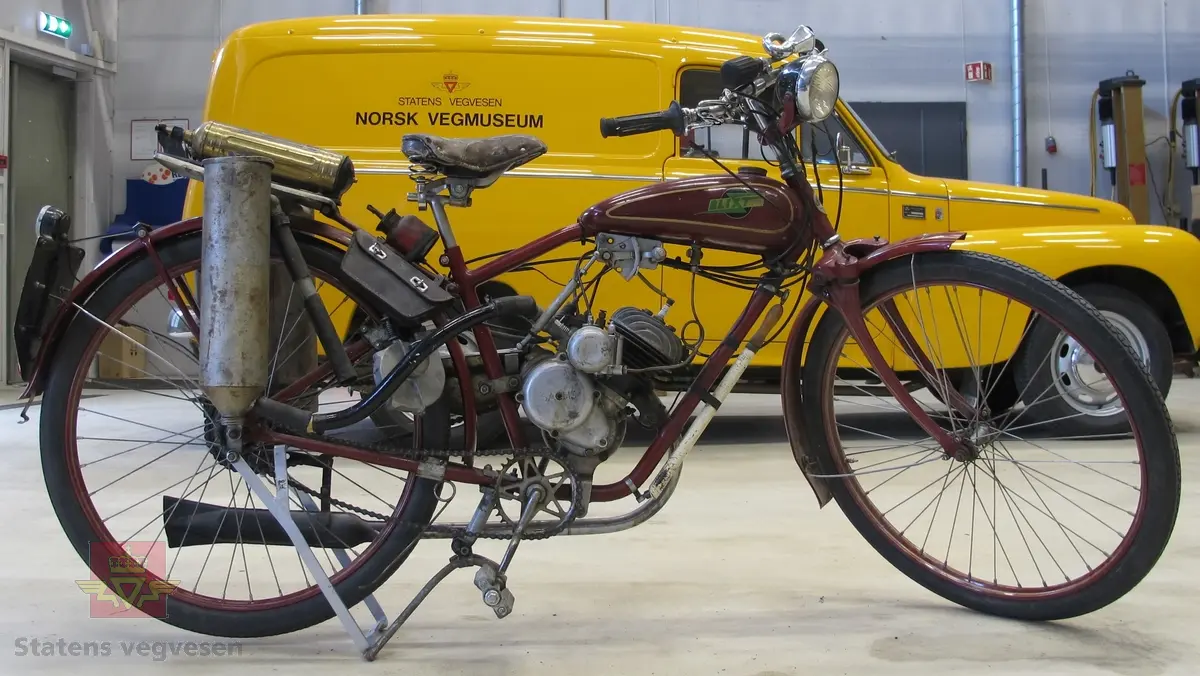 Blixt 98 cm3. Rød (vinrød), motorsykkel med pedaler, forbrenningsmotor og vedgassgenerator. 
Motorsykkelen er en BLIXT lettvekts motorsykkel fra 1936 med en 98 cc, en-sylindret totaktsmotor av fabrikat Fichtel & Sachs som yter 2,5 hk og går på bensin.
Generatoren er av fabrikat Åsbrink, type Sperco lI, og laget primært for bruk med trekull. Virkningsgraden er ca 0,4 med "godt køl", det vil si en 2,5 hk motor kan under gunstige omstendigheter teoretisk utvikle ca 1 hk. Kullet skal knuses til biter av størrelse 5-15 millimeter, og oppfyringen er svært omstendelig. I teorien skal man kunne kjøre ca 10 km på "en fyring".
Motorsykkelen har 2 gir og veier 73 kilo.
Den er 72 cm bred, 210 cm lang, og ...høy...
På hele sykkelen er det 1 sitteplass.
Det er montert pumpe til dekkene på ramma og et brannslukkingsapparat bak på sykkelen.