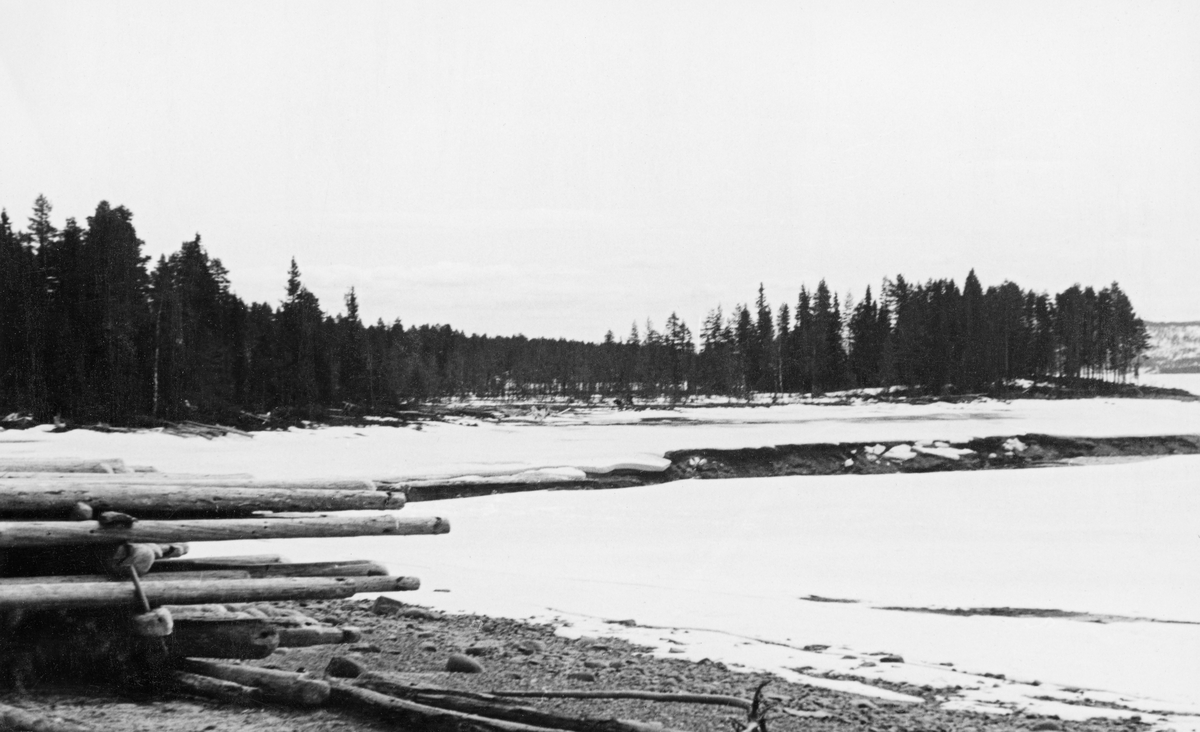 Elva Tverrenas utløp i Osensjøen i Åmot.  Stedet kalles Tverrenhullet.  Bildet er tatt 10. april 1941.  På dette tidspunktet var elva isfri, men sjøen var fortsatt is- og snødekt.  Til venstre i forgrunnen ses noe av en stabel med lensetømmer.  Når fløtingssesongen kom i gang ble dette virket brukt til å samle opp tømmer som skulle slepes med båt til Valmen i den nordvestre enden av sjøen.  Derfra ble virket sluppet i elva Søndre Osa og fløtt videre på Rena og Glomma. I 1941 var det innmeldt 90 366 tømmerstokker til fløting i Brøa, Ulvsjøene, Ena og Tverrena. Alt dette tømmeret, snaut 18 prosent av det som skulle fløtes i Osenvassdraget dette året, ville nå sjøen her ved Tverrenhullet. Denne vinteren og våren var sjøen uvanlig sterkt nedtappet på grunn av Glommen og Laagens brukseierforenings regulering av Osensjøen, noe som forsinket den påfølgende fløtingssesongen kraftig. Fotografiet er antakelig tatt for å dokumentere konsekvensene av nedtappinga.
