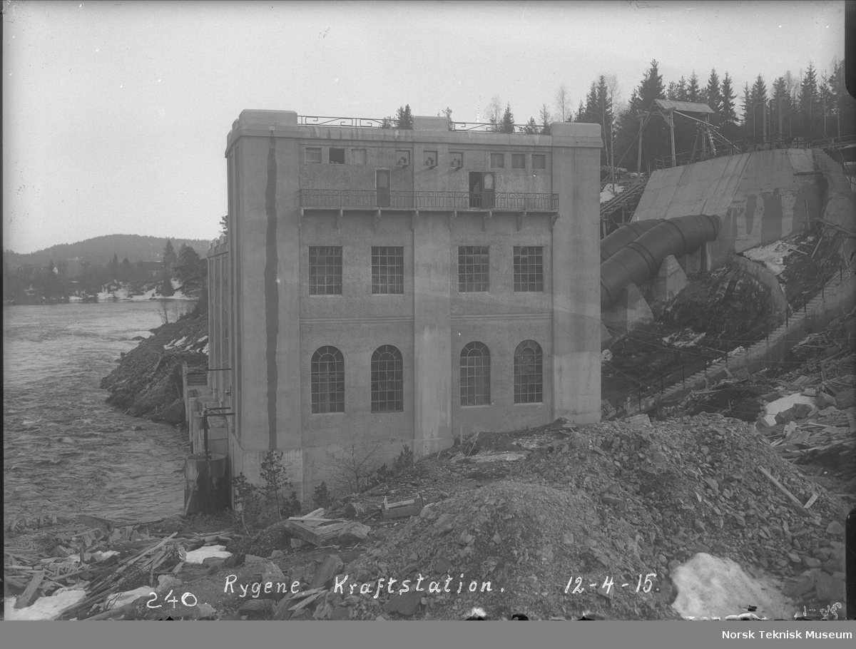 Eksteriørbilde av Rygene kraftstasjon med uttak og rørledning : kraftstasjonen eies av A/S Rygene Tremassefabrikker og ble bygget i 1913-14, senere ble det bygget ytterligere to kraftstasjoner tilhørende samme anlegg