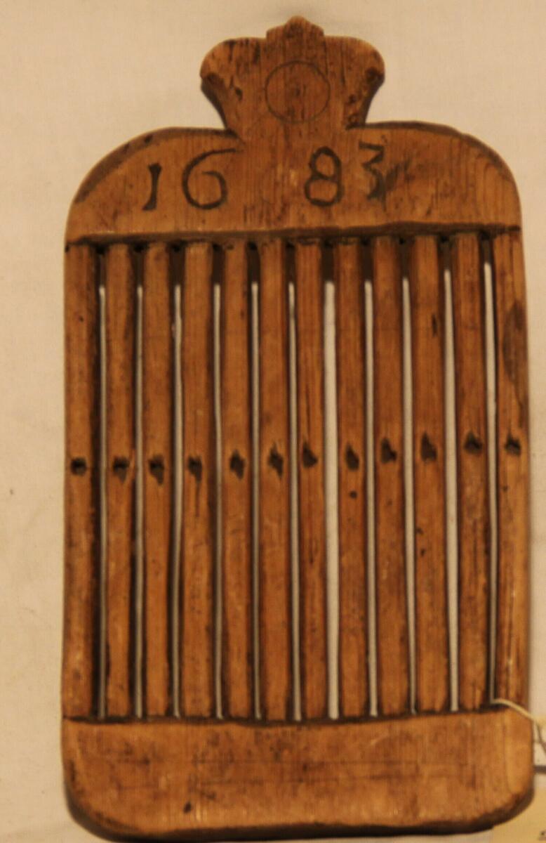 "Bandvävsked av trä, som skissen, med profilerat överstycke på ena sidan inskuret "1683", på den andra "K I D". 12 tinnar med hål i mitten. - Höjd 21 cm. Bredd 11,2 cm. - Gåva av Jonas Näslund." (skiss) (ur lappkatalogen, Arvid Enqvist 1936)
