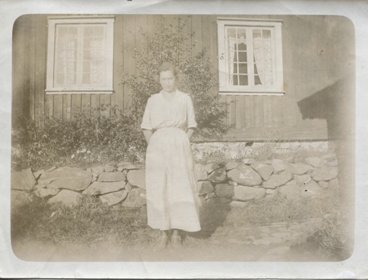 En okänd kvinna står framför ett hus, okänd plats och årtal. Foto från Sagered-album.