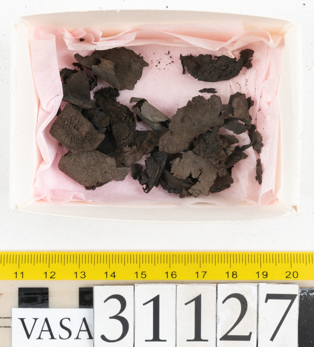 Delar och fragment från sko; tre sulor, en holtrand, en klacklapp, en klacklapp eller ett inlägg samt ett 40-tal delar och mindre fragment från skoöverdel och skobotten.
Sula fyndnummer 31127 har kvarsittande tråd. På sulans ovansida finns intryck av bindtråden.  Sula fyndnummer 31127:1 har kvarsittande träpligg och tråd. I tåpartiet finns en laglapp. Sulans hälparti är avskuret, eventuellt avbrutet.  Sula fyndnummer 31127:2 har ett fragmentariskt hälparti. På sulans ovansida finns intryck av bindtråd. Holtrand fyndnummer 31127:3 har kvarsittande tråd. På klacklapp fyndnummer 31127:4 finns hål efter träpligg. På klacklapp, eventuellt inlägg, fyndnummer 31127:5 finns kvarsittande tråd.