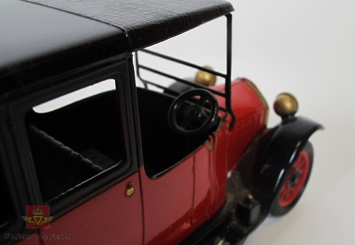Rød modellbil med svart tak og hjulbuer. Festet til reservehjulet og selve hjulet mangler.
