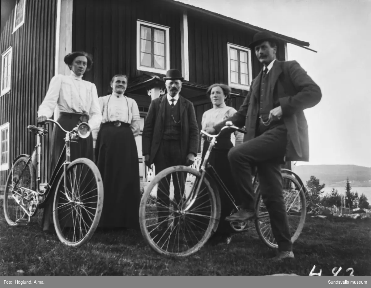 Fem personer, två med cyklar, utanför ett högt beläget bostadshus.