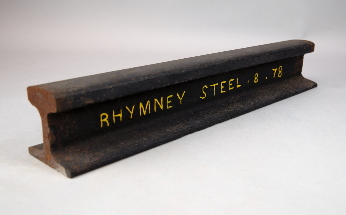 Vingnolräl av järn med huvud, liv och flatbottnad fot. På ena långsidan står det "RHYMNEY STEEL . 8 . 78", senare målad med gul färg.