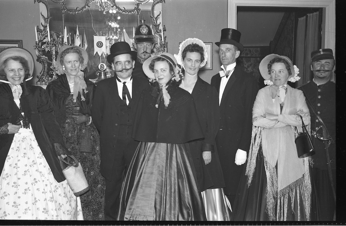 En grupp kvinnor och män klädda likt tidigt 1900-tal, troligen på Ribbagården i Gränna. Kvinnan till vänster är Dagmar Petri, mannen i hög hatt är Bertil Ander.