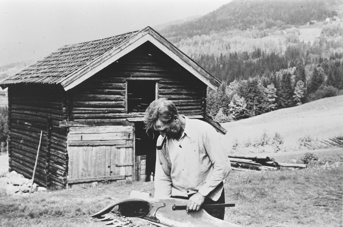 Lars Bjerkmann reparerer slåmaskinen. Foran vognskjulet på Teige i Eggedal, 1954.