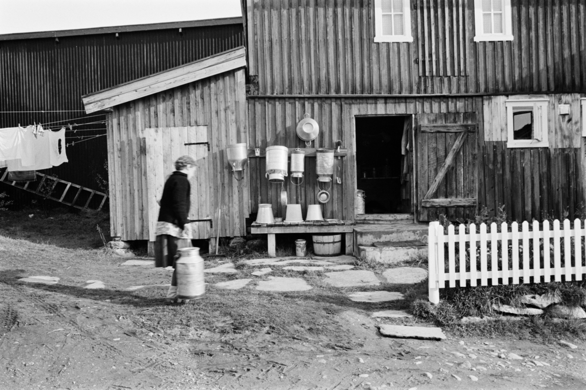 En kvinne står med melkespann i et gårdsrom på Røros.