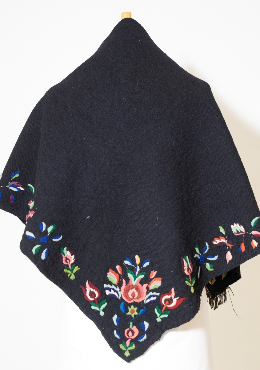Kvadratisk sjal med blomsterborder brodert med ulll. Ulike broderimønster på det to snippene når sjalet brettes. Påsydde frynser på ene hjørnet.