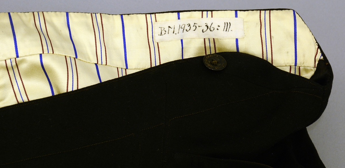 Uniformsbukse. Nr. 111: av svart klæde; gullborde som fyrre nr. (ein rank av eikeblad og eikekonglar/eikenøtar).Fra protokoll. Uniformsbuksen tilhører livkjole TGM-BM:095.