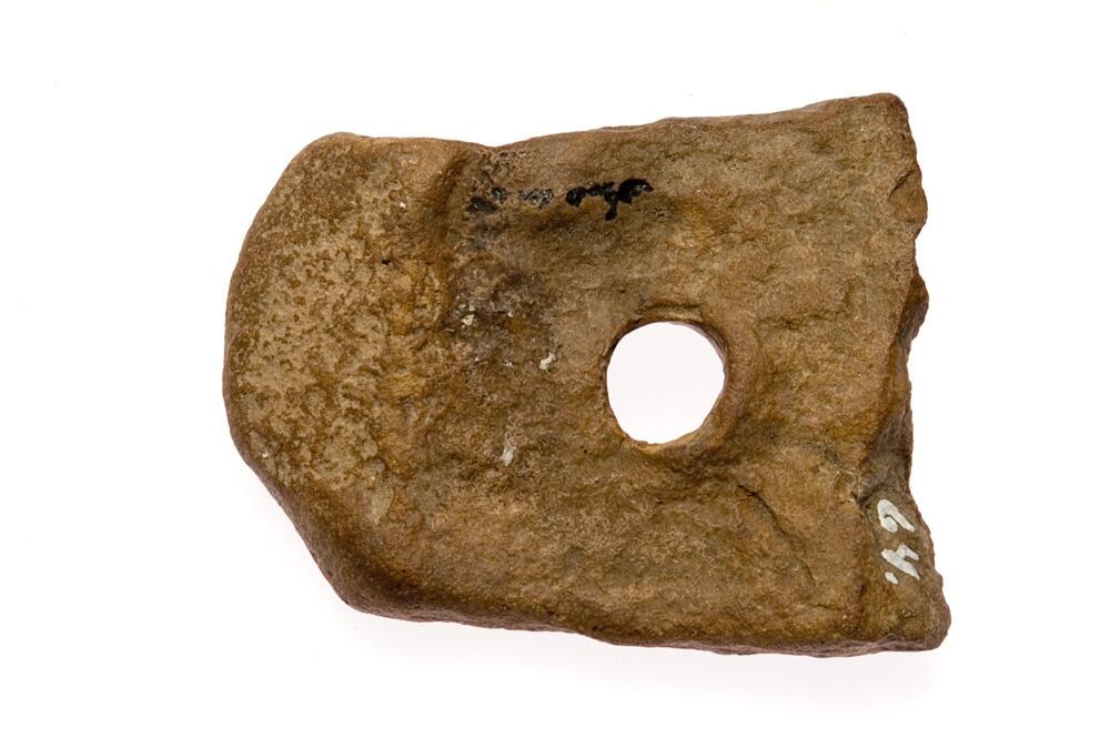 Nätsänke. Flat sten med hål, av brun stenart. Avslagen. Med runt hål.