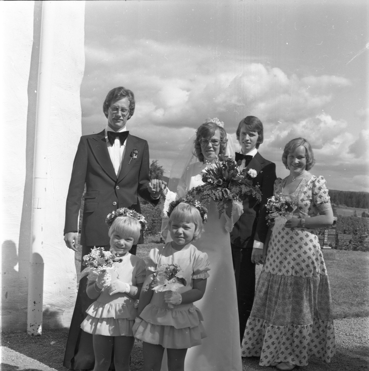 Ett brudpar med tärnor och marskalk står utanför Ölmstad kyrka.