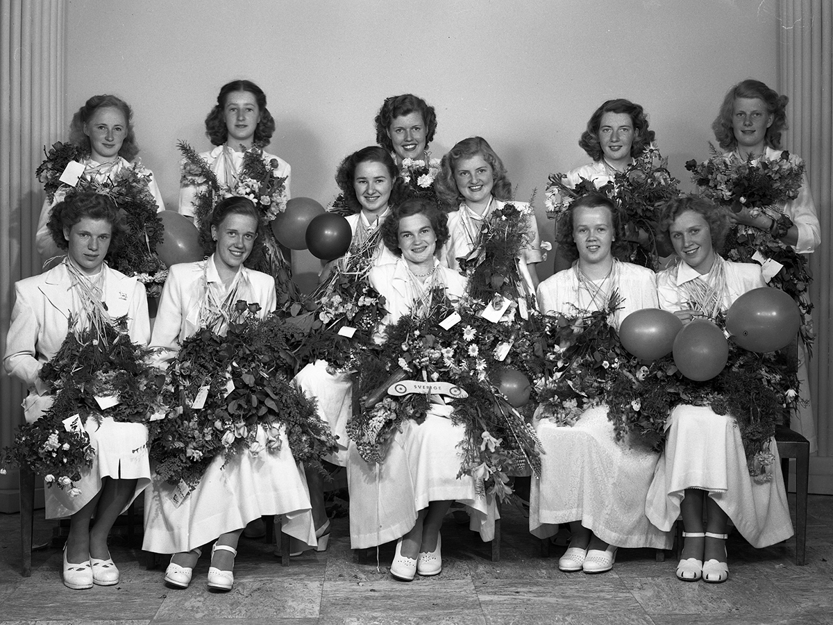 Flickskoleexamen 1949 vid Varbergs flickskola. Flickorna är samlade för fotografering med sina blombuketter och ballonger inomhus.