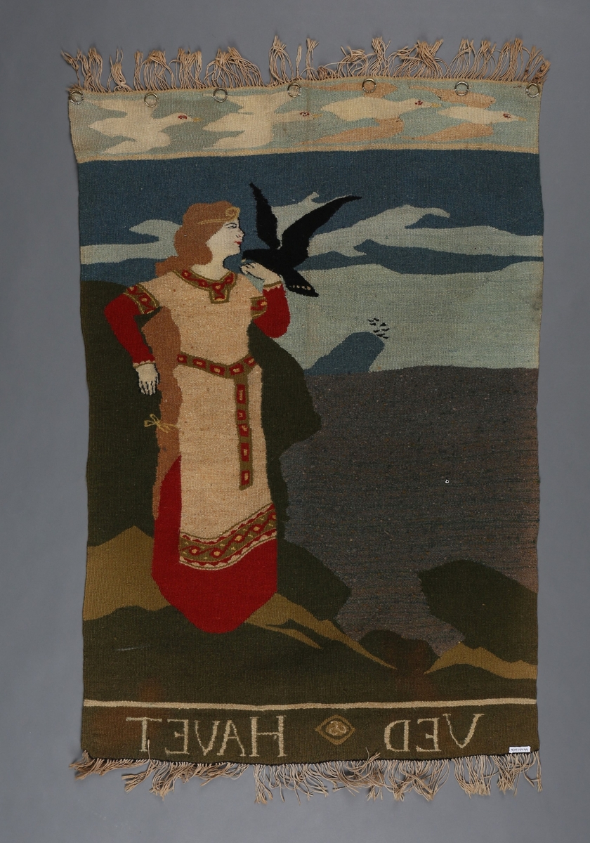 Kvinneskikkelse står til høgre i vevnaden att ved havet med ein svart fugl på handa. Frise øvst på teppet med ei fugl i 4 livstadier, frå ung til vaksen.