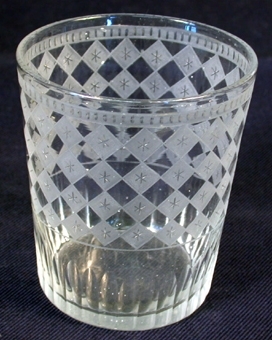 Cylinderformat dryckesglas av genomskinligt glas. Utsidans yta dekorerad med frostat rutermönster och andra mönster. Samhör med inv.nr. 34678.