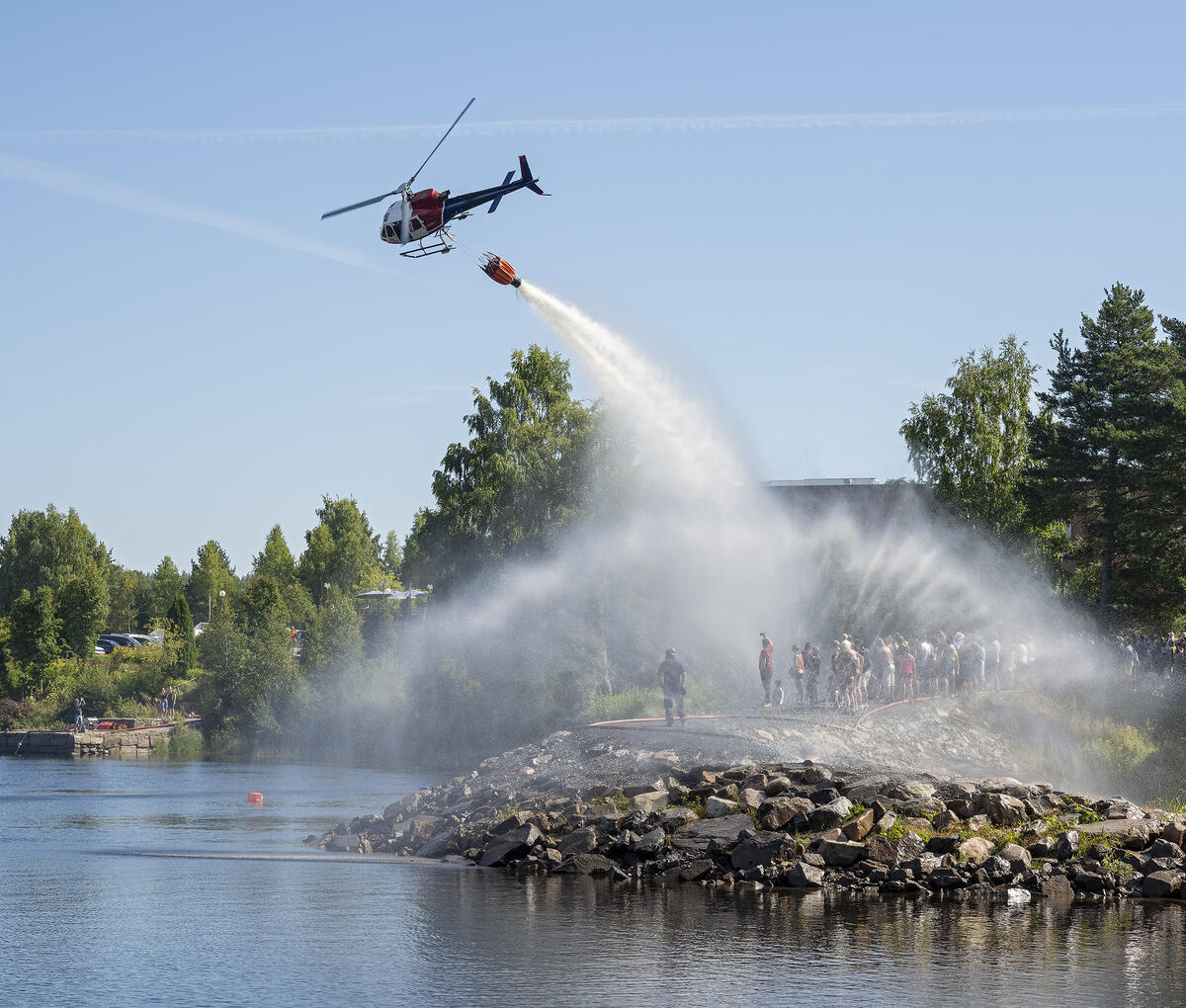 Bildet viser demonstrasjon med skogbrannhelikopter under De nordiske jakt- og fiskedagene 2022. Publikum følger med på piloten som slipper vann fra en dunk under helikopteret