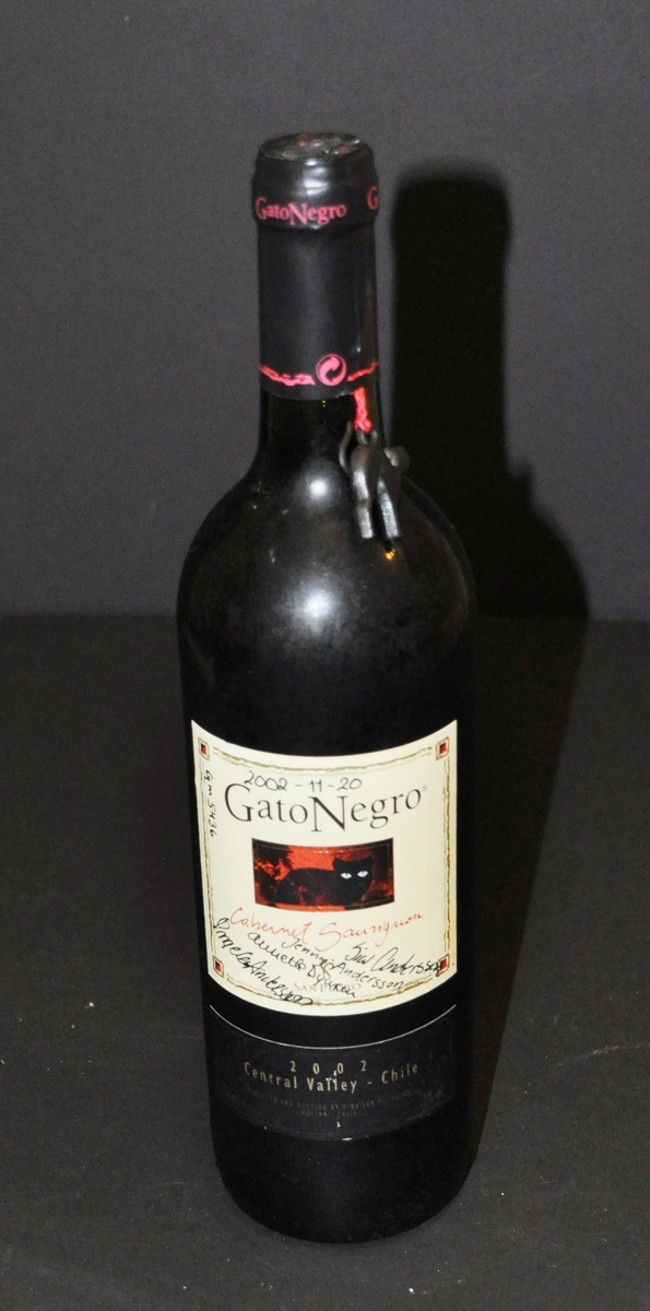 En flaska med rödvin. Det finns en etikett på flaskan med en svart katt.