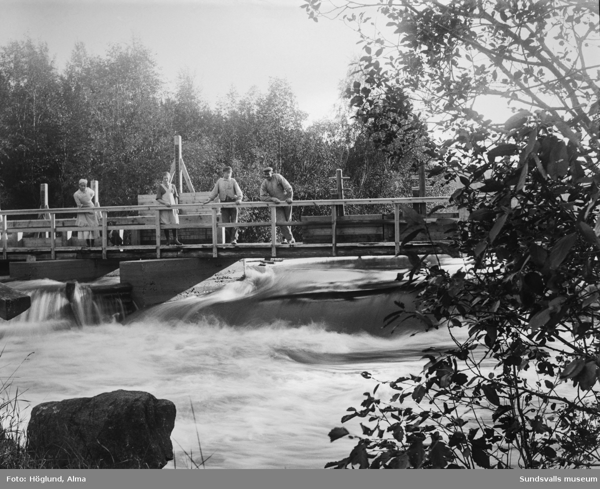 Bro och fördämningar, möjligen kvarnbygge, i Fanbyån. Mjölnarparet Sanna (till vänster) och Emil (till höger) Eriksson. Däremellan Märta Björk och en oidentifierad pojke.