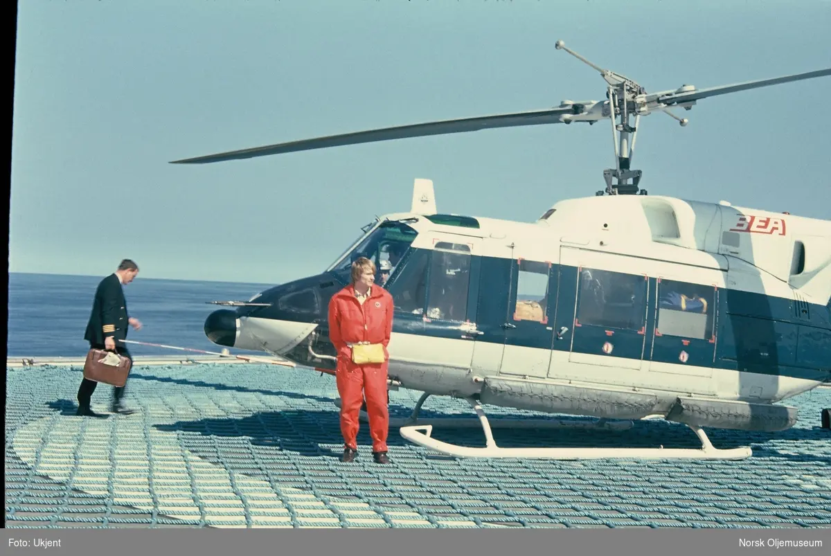 En kaptein og en offshore-arbeider i arbeidstøy utenfor et helikopter på en heliport offshore.