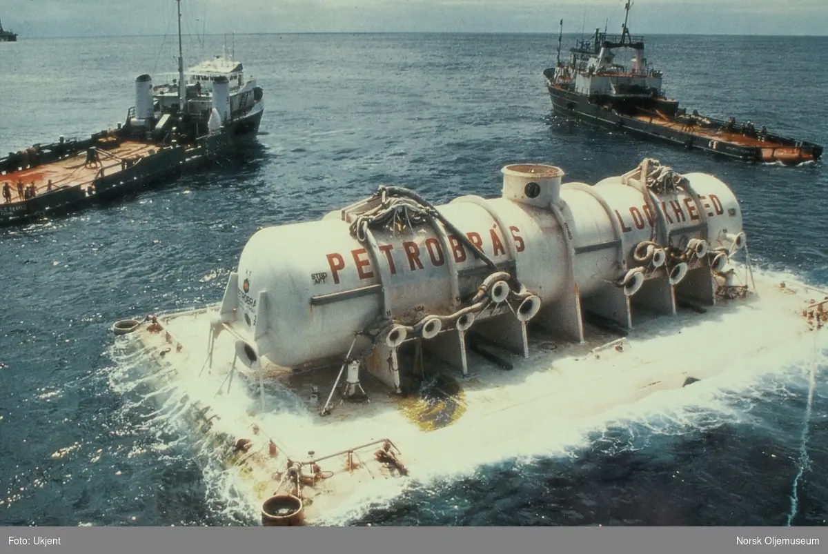 En tank ligger på havoverflaten med forsyningsskip rundt. På tanken står det "Petrobras" og "Lockheed".