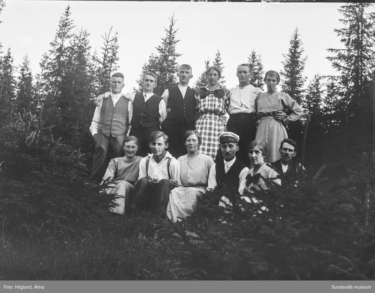 Två gruppbilder med tolv personer i en skogsbackeSamma personer på båda bilderna förutom nummer fyra längst fram. På bild nummer två sitter där Helmer Höglund, övriga är oidentifierade.