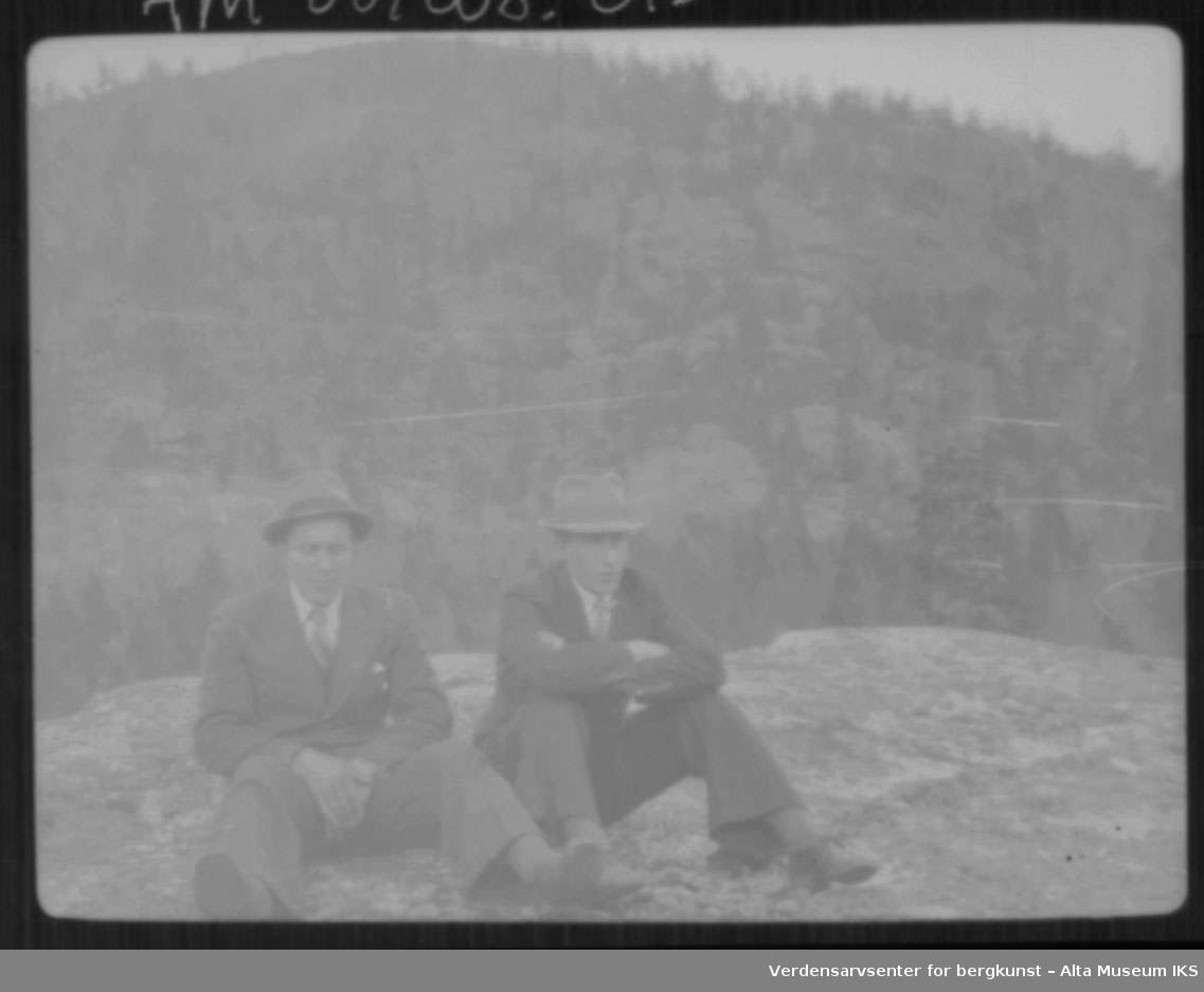 2 menn med dress og hatt sitter på et fjell.
