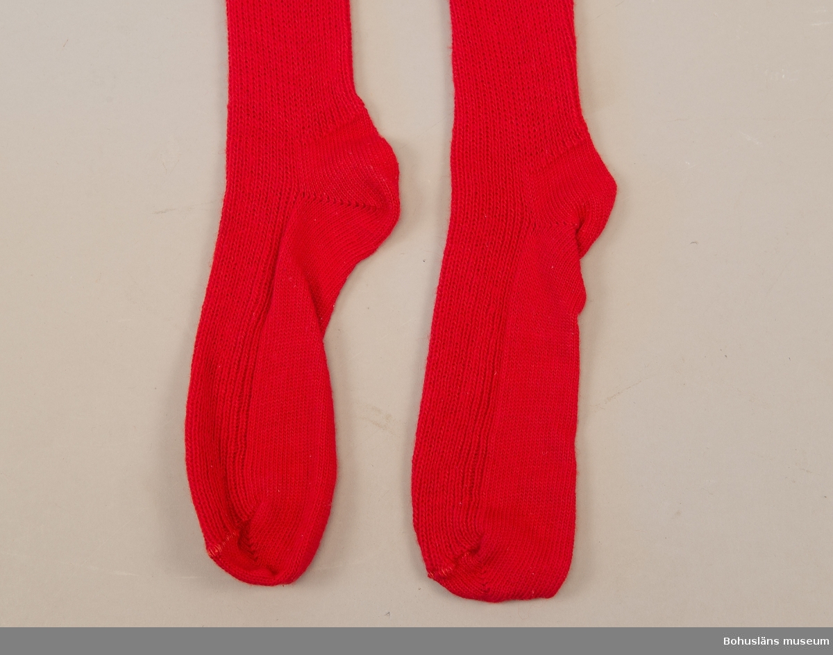 Del av bohusdräkt.
Enfärgad resårstickad röd strumpa handstickad av ullgarn, slätstickning under foten. 
För att hålla strumpan på plats ska möjligen ett strumpeband knytas över knäet.
Samhör med UM033951.