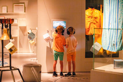 To barn trykker med hodetelefoner står foran en skjerm i utstillingslokale.