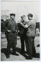 Fotografi av to krigsfanger som står og snakker med en lege 