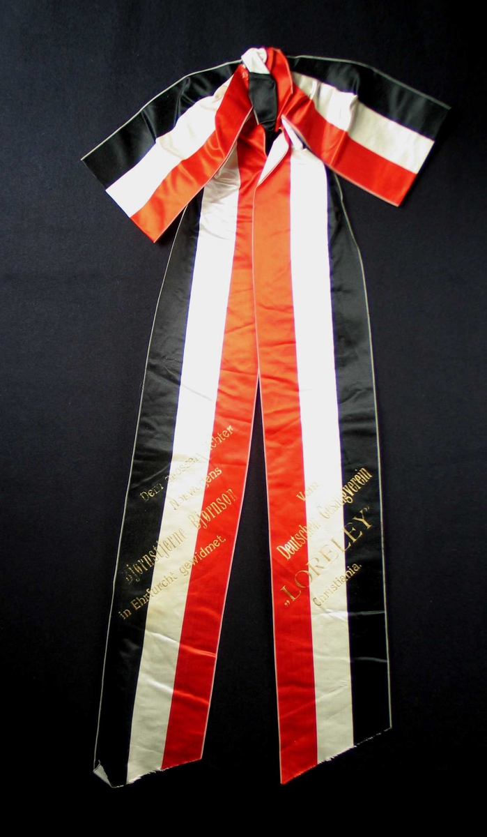 Begravelsessløyfe i rød, hvit og svart silke med tekst i gull.
