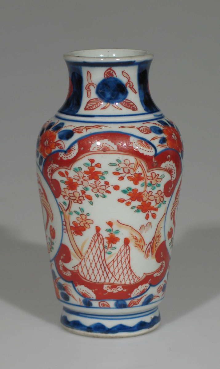 Hvit vase i porselen med dekor i blått og rustrødt. Vasen er urneformet.