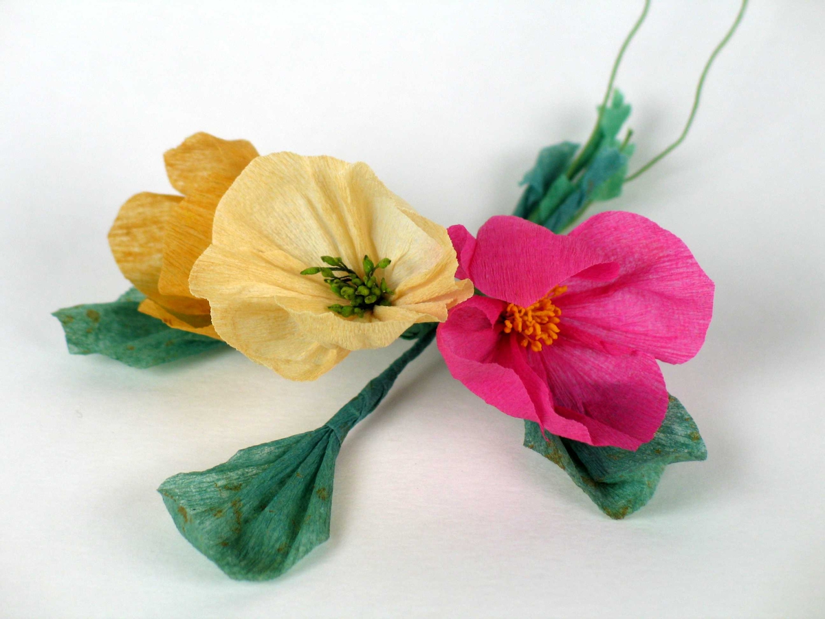 Tre små blomsterbuketter laget i kreppapir. Ligger i en pappeske med innskrift på lokket.