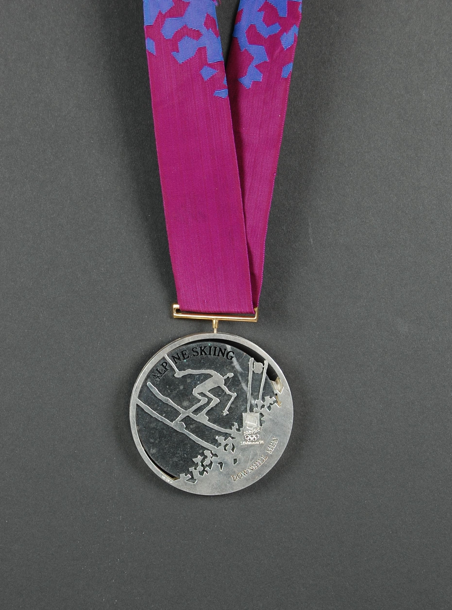 Rund medalje i valør sølv. I dekoren på den ene siden er det et piktogram av en alpinist, og motivet er hentet fra LOOCs designprogram. Det er også stemplet logo for de olympiske leker på Lillehammer i 1994. På den andre siden inngår de olympiske ringene som en del av dekoren.