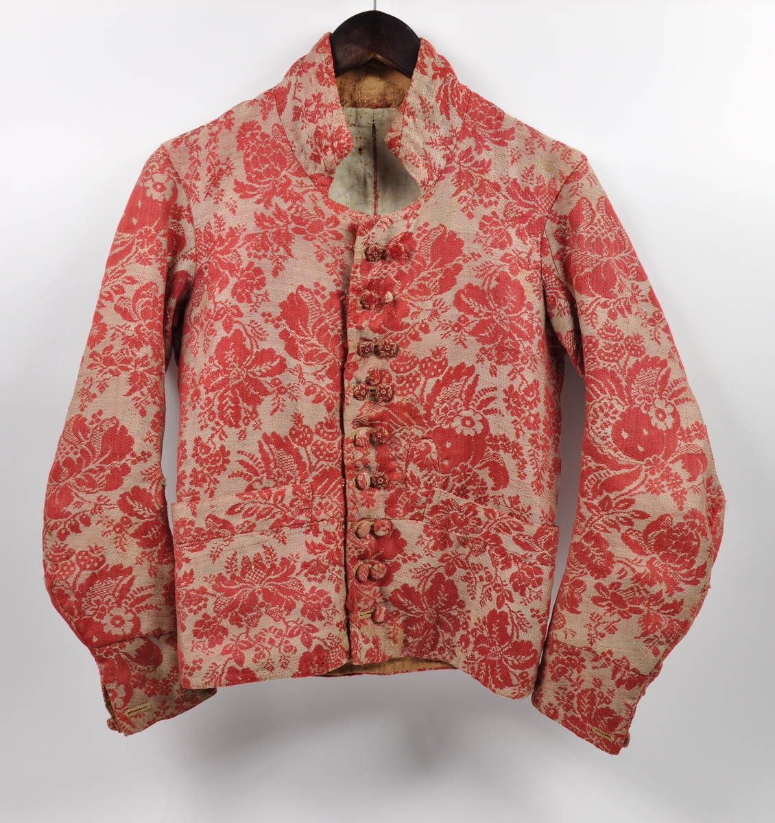 Håndsydd vest av ulldamask, fôret med to typer linstoff. Ryggsømmene er sydd med spilesøm. Vesten har ståkrage, dobbel knapphullrad (18) , trekte knapper (to ulike stoff) (16) - to mangler. Det vil si ni knapphull  og knapper på hvert forstykke. Knapphullene er sydd med lintråd.
To sidelommer. Knapp og knapphull nederst på ermene.