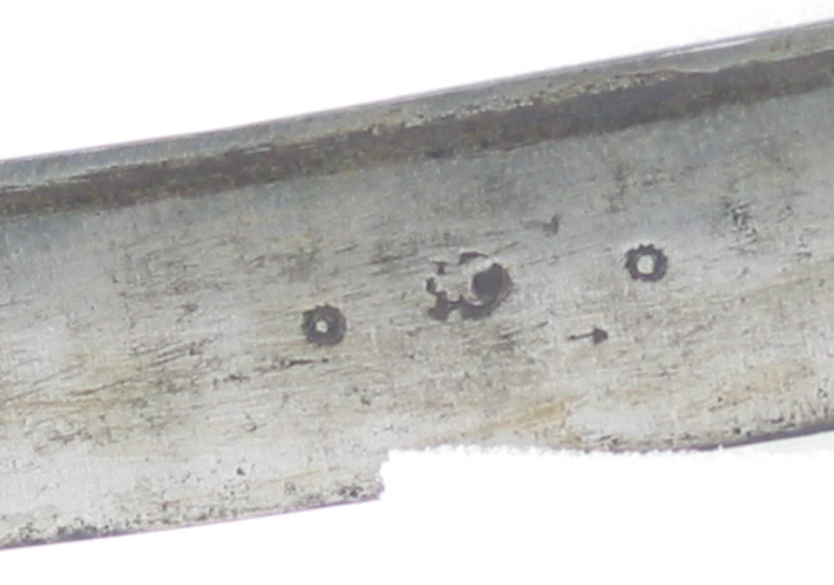 Pyramideformet knapp med strekdekor. Asymmetrisk kurvfeste med to sidebøyler( øverste avbrukket )med riflede fortykkelser på midten. mellom håndbøylen og kurvens ytterkant. Innsiden har en  sidebøyle. Kurvens basis er på utsiden en kvadratisk parérplate med to hjerteformede gjennombrytninger. På innsiden er det en klingebrekker og tommelbøyle. Opp og nedbøyde parérstenger med riflede fortykkelser på endene.
Tregrep med nyere jerntrådvikling.
Enegget krum klinge med 3 hull ipå klingspissen og en smal hulslipning på ryggsiden.Tre smedmerker på venstre side. 