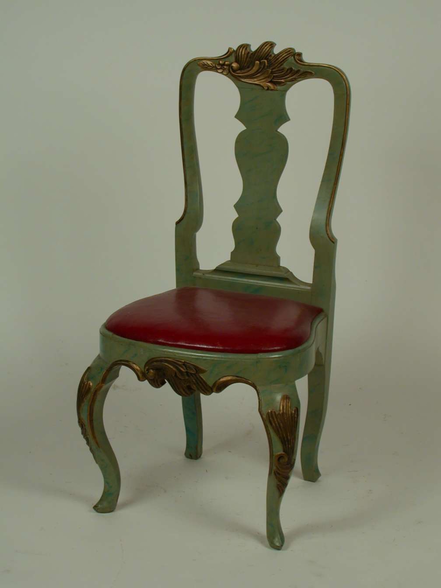 Lasert grønn stol med løst sete med polstring dekket med lær. Læret er rødt. Stolen har svungne forben med bronsert dekor på knærne. Stolen er dekorert med bronsert bladverk på sarg og toppstykke.