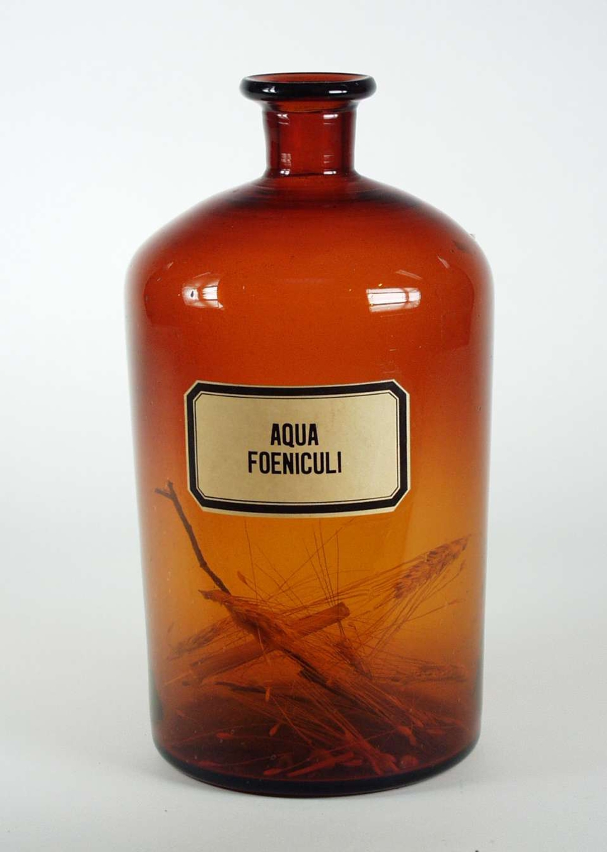 Apotekerflaske i brunt glass. Den har etikett påtrykket: Aqua Fueniculi.