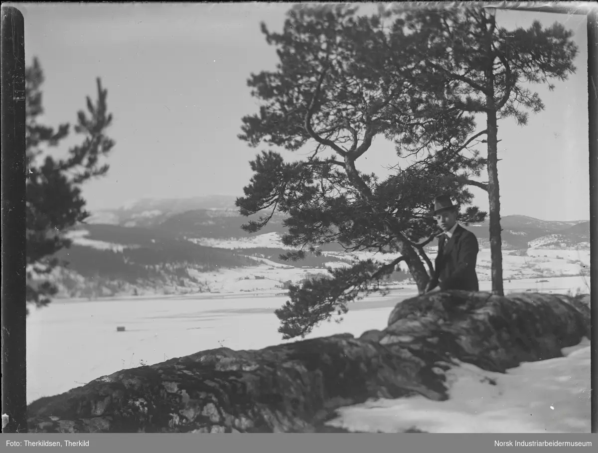 Mann sittende på fjellkant. Utsikt mot Heddalsvannet og Vestsida.