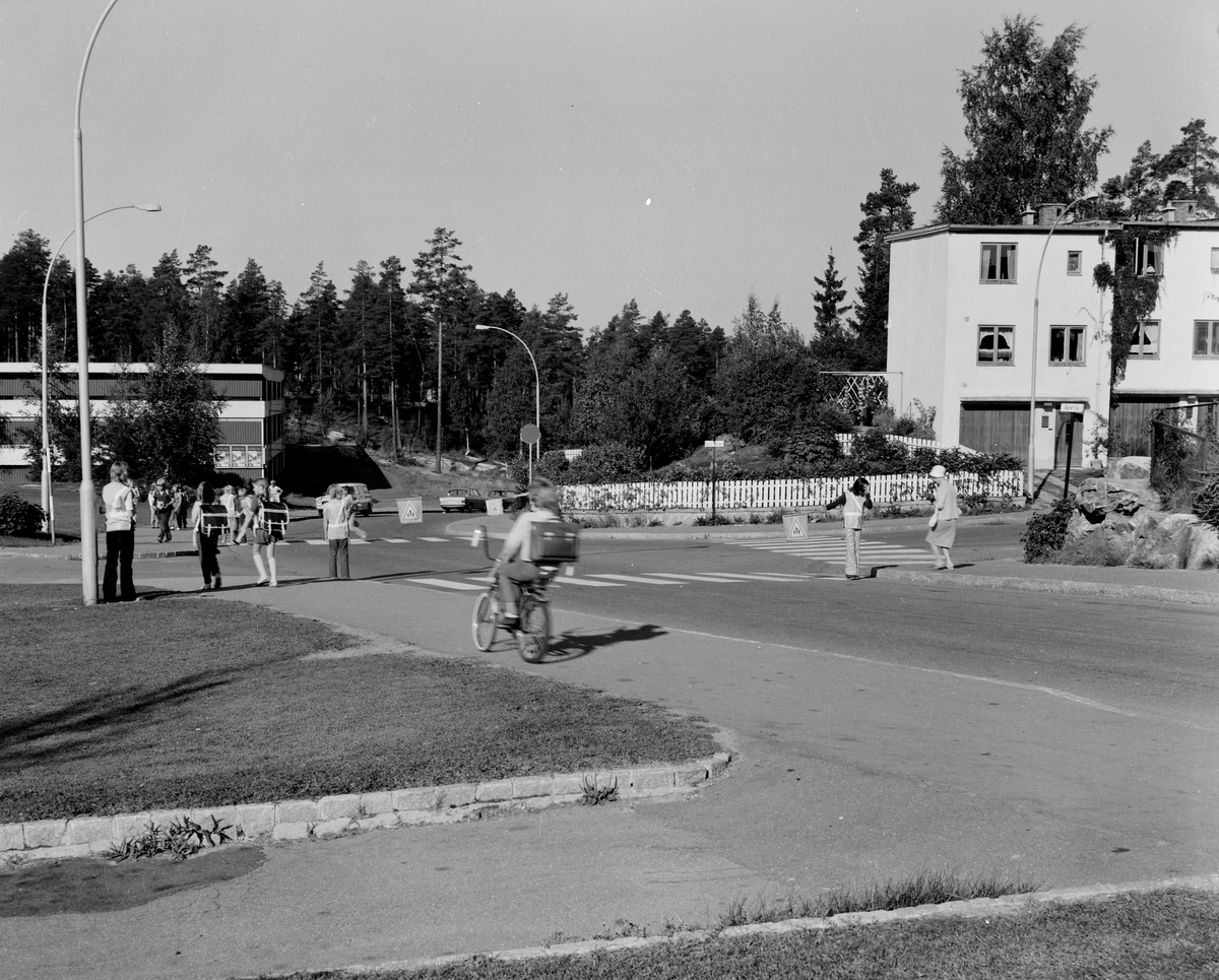 Foto av veikryss på Bøler i Oslo. Barn på sykler, eldre, en skolepatrulje kontrollerer trafikken.