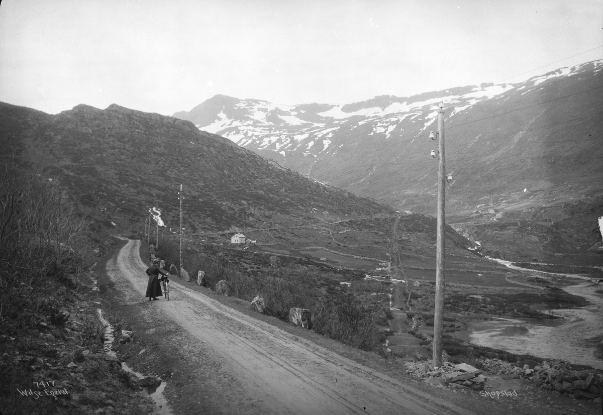 Kvinne på tur med sykkel. Ny og gammel vei ved Skogstad, Vang i Valdres. Fotografert i mai 1907.